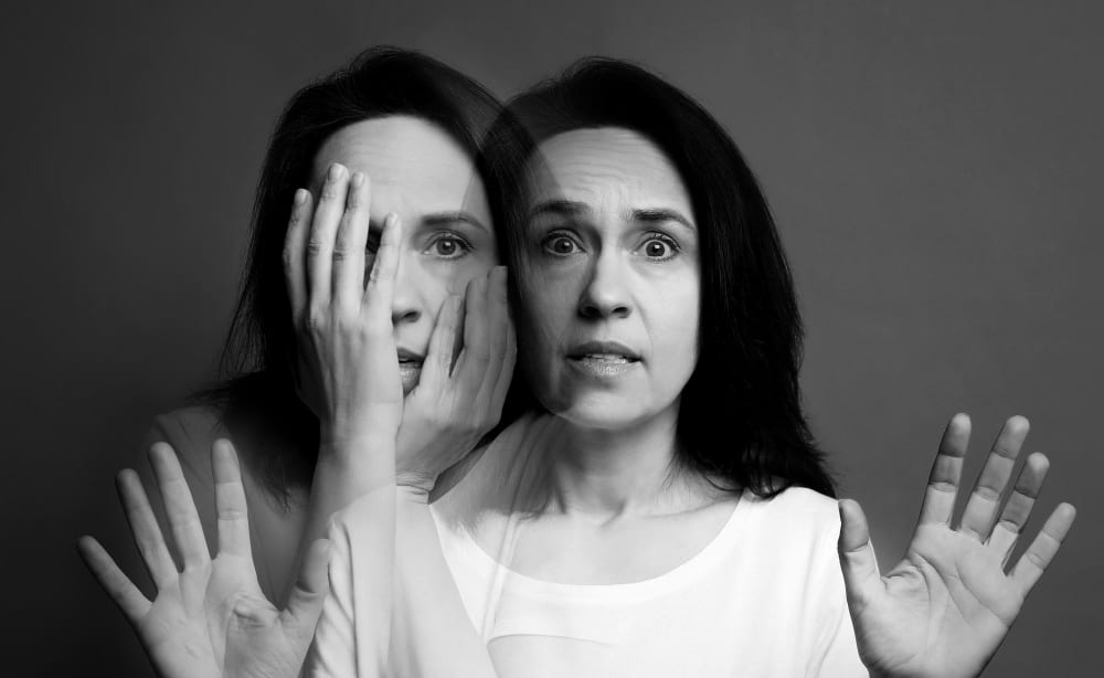 Portret alb-negru cu dublă expunere: aceeași femeie acoperindu-și fața cu mâna și, suprapus, privind speriată în față